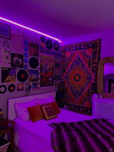 a bedroom with purple lighting and lots of pictures on the wall above the bed,