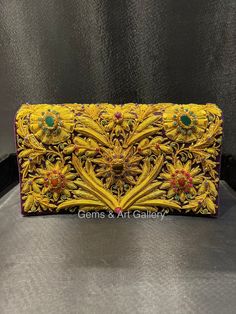 a yellow and pink embroidered clutch bag with flowers on the front, sitting on top of a metal surface