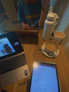 a laptop computer sitting on top of a wooden table next to a cup of coffee