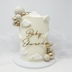 a white and gold baby shower cake with clouds on it's side that says, baby congratulations