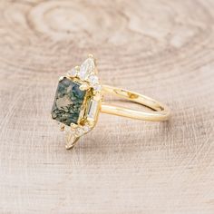 a gold ring with a green and white stone surrounded by diamonds on a wooden surface