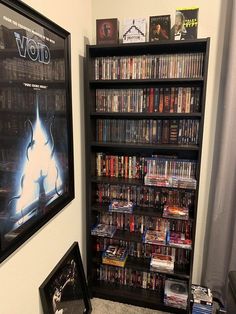 a book shelf filled with lots of movies next to a framed movie poster on the wall