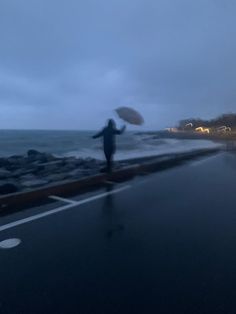 a person holding an umbrella standing on the side of a road next to the ocean