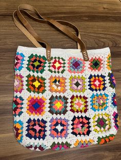 a multicolored crocheted bag sitting on top of a wooden table next to a brown leather strap