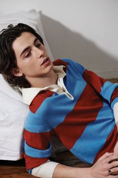 a young man laying on top of a bed next to a white pillow wearing a blue and red striped shirt