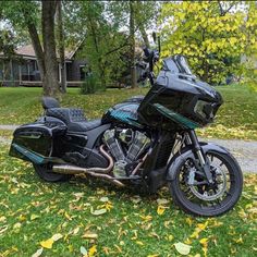 a black motorcycle parked on top of a lush green field next to trees and leaves