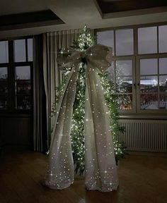 a decorated christmas tree with lights in the corner and a large bow on it's side