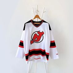 a jersey hanging on a rack in front of a white wall with a black and red stripe