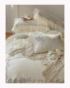 a bed with white comforters and pillows on top of it next to an open book