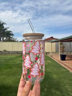 someone is holding up a glass cup with trees on it in the grass near a fence