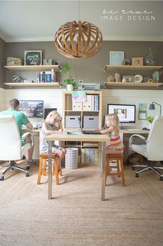 two people sitting at a desk in front of computer monitors and laptops with shelves above them