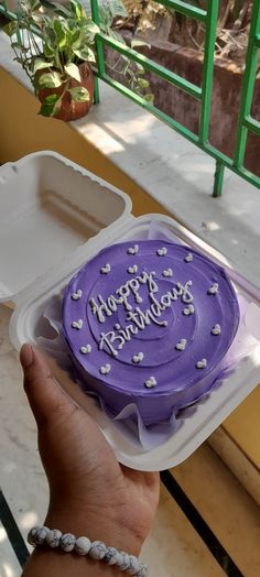 a purple cake in a plastic container with white hearts on the top and happy birthday written on it