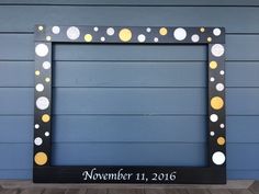 a black frame with yellow and white polka dots on it, next to a blue wall