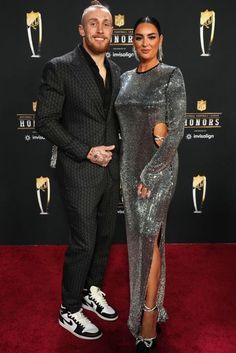 a man and woman posing on the red carpet at an awards event with trophies in the background