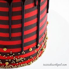 a red and black striped cake with gold decorations on the top, topped with chocolate drizzles