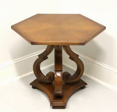 a wooden table with an octagonal top and carved designs on the sides, against a white wall