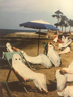 some people are sitting in lawn chairs on the beach with ghost faces painted on them