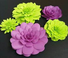 paper flowers arranged in different colors on a black table top with one large pink, one green and one small purple