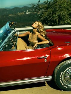 a woman sitting in the driver's seat of a red car