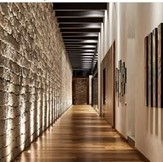 a long hallway with wood floors and stone wall covering it's walls, leading to another room