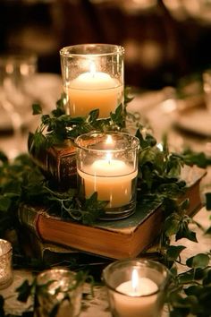 candles are lit on top of an old book with greenery and ivy around it