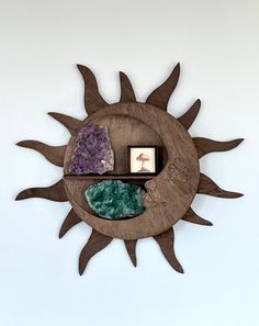 a metal sun with some rocks in it on a white wall and two pictures hanging from the side