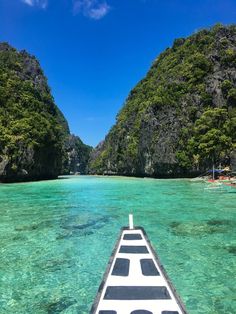 the bow of a boat in clear blue water with green mountains and trees behind it