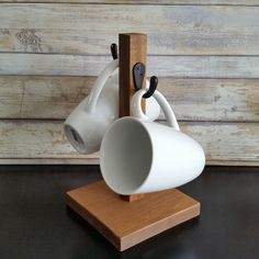 a white coffee cup is hanging on a wooden stand with two black handles and a brown base