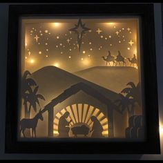 paper cut nativity scene displayed in frame with light bulbs on the wall behind it