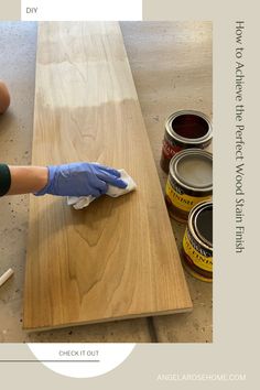 a person in blue gloves wiping down some paint on a wooden table with two cans of paint next to it