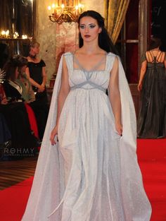 a woman is walking down the red carpet wearing a white gown and cape with silver sequins on it