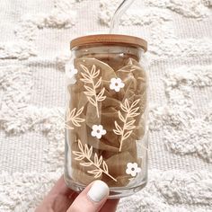 a hand holding a glass jar filled with brown and white flowers on top of a lace covered tablecloth