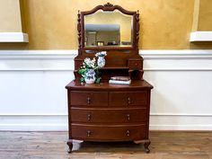 a wooden dresser with mirror and flowers on top