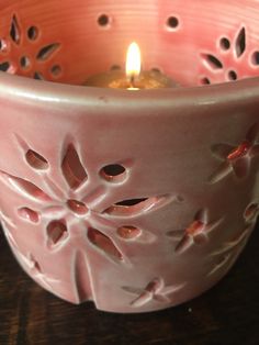 a pink candle holder sitting on top of a wooden table next to a lit candle