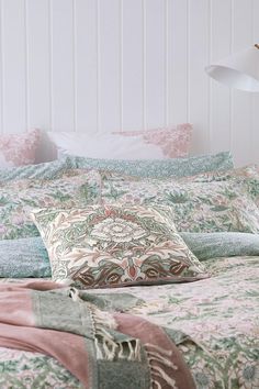 a bed with pink and green comforters on top of it next to a lamp