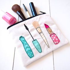 an embroidered pouch with makeup brushes and lipstick on it