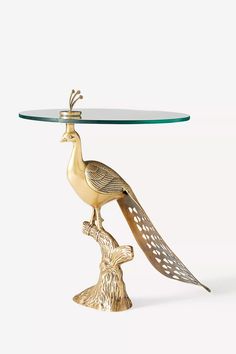 a glass topped table with a gold bird on it's leg and a metal base