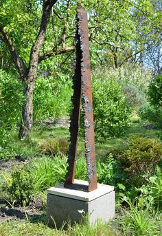 a metal sculpture in the middle of a grassy area with trees and bushes behind it