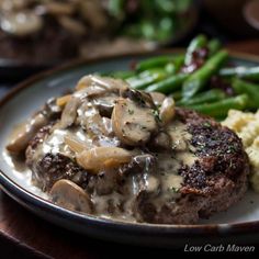 a plate topped with meat and potatoes covered in gravy next to green beans