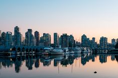 the city skyline is reflected in the calm water at dusk, with boats moored to shore