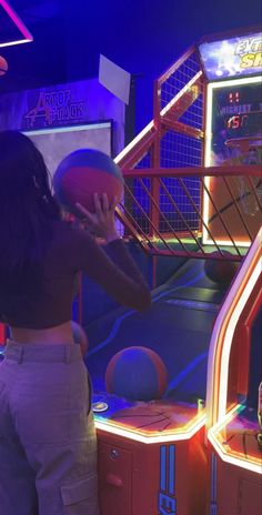 a woman is playing with a basketball in an indoor pinball game room at night