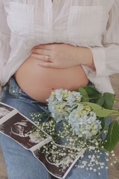 a pregnant woman sitting on the ground with her stomach exposed and flowers in front of her belly