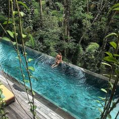 a woman is swimming in a pool surrounded by greenery and wooden decking area