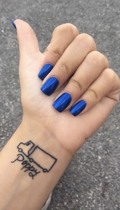 a woman's hand with blue nail polish on it and a black outline tattoo