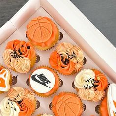 cupcakes decorated with orange and white icing are in a box on a table