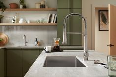 a kitchen with green cabinets and white countertops has a stainless steel faucet