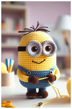 a crocheted minion is holding a knitting needle and looking at the camera