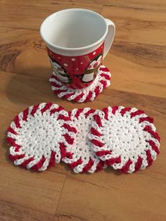 three red and white crocheted coasters next to a coffee cup on a wooden table