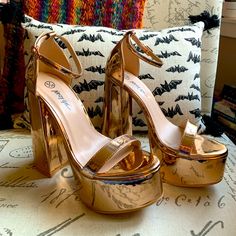 a pair of gold high heeled shoes sitting on top of a bed next to a pillow