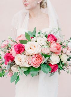 a bride holding a bouquet of pink and white flowers on her wedding day in front of a pink wall